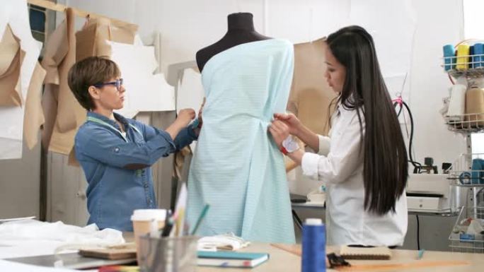 女裁缝将织物钉在人体模型上并讨论服装
