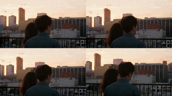 日落时，屋顶露台上的夫妇的后视图俯瞰城市天际线