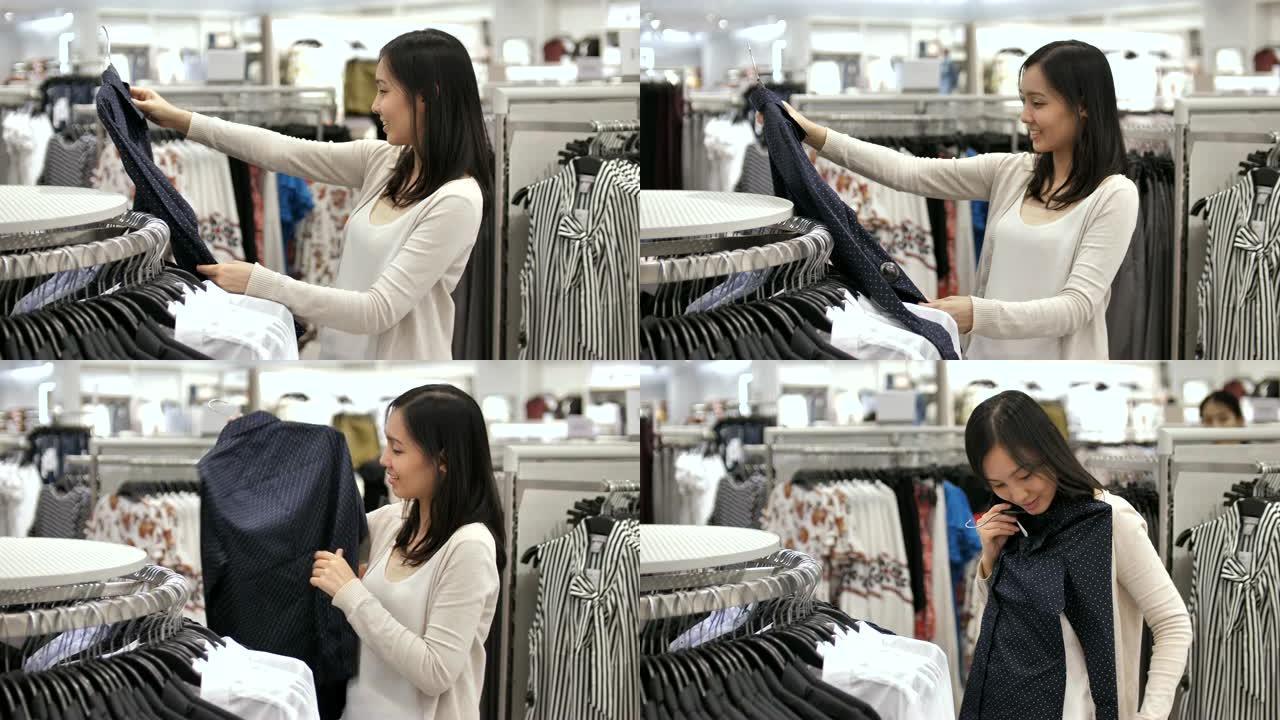 年轻的亚洲妇女在服装店的架子上选择购物衣服