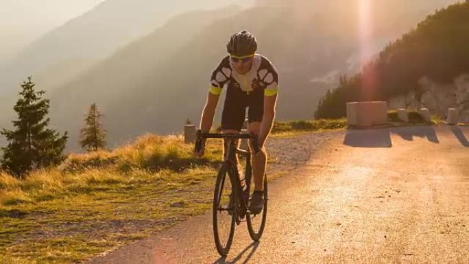 道路自行车手在日落时爬坡时站起来