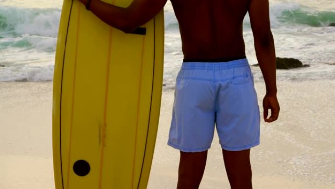 非洲裔美国男性冲浪者站在沙滩上的冲浪板后视图4k