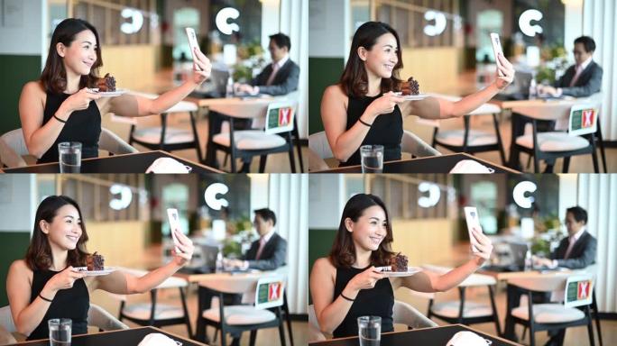一名亚洲中国女性在自助餐厅茶歇期间享受甜点巧克力蛋糕，同时练习社交距离自拍手机信息