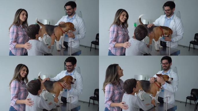 英俊的兽医在与女主人和她的儿子交谈时检查狗