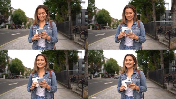 伦敦街美丽的年轻女子戴着耳机听音乐，看着智能手机微笑