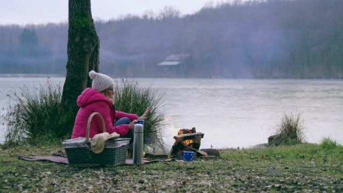 女士女士在斯洛文尼亚Prekmurje的秋季湖畔篝火旁暖手
