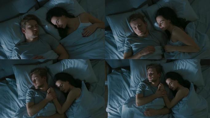 晚上的俯视图床: 迷人的年轻夫妇睡在一起，互相拥抱。早晨的第一缕阳光照亮了窗户的房间