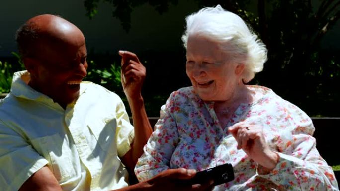 在养老院4k花园中使用手机的活跃混血老年夫妇的前视图