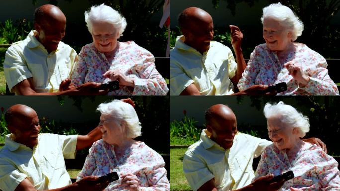 在养老院4k花园中使用手机的活跃混血老年夫妇的前视图