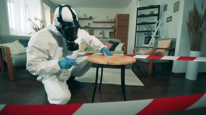 一个穿着危险品的人用消毒剂打扫桌子。covid 19大流行期间使用的抗菌消毒剂。