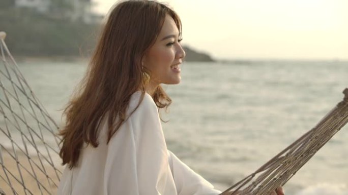 美丽的年轻亚洲女子在吊床上放松的肖像，在海滩上享受她的暑假。
