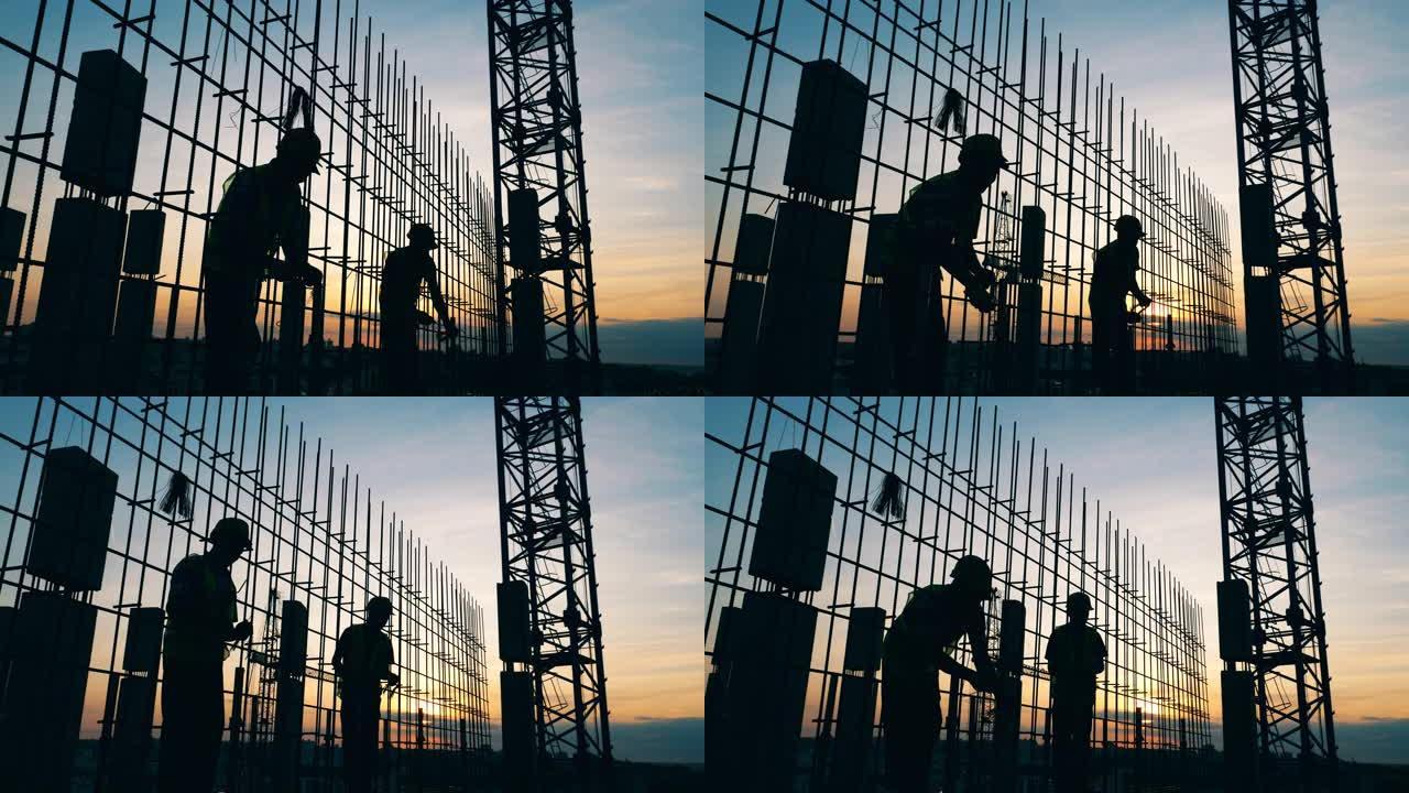 男性工人在日落背景上建造房屋。