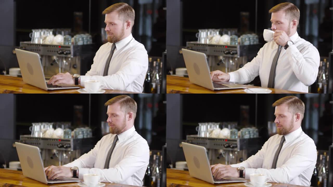 商人在咖啡店的酒吧柜台使用笔记本电脑并喝咖啡