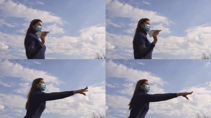 戴面具的年轻女子正在户外扔纸飞机。慢动作