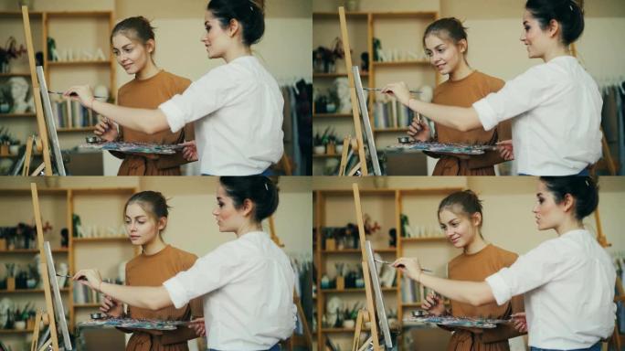 经验丰富的美术老师正在教她的学生用展示新技术的油画绘画。女孩在漂亮的现代工作室微笑着享受课堂。