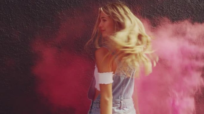 美丽的年轻金发女孩与粉红色烟雾弹对着黑墙跳舞