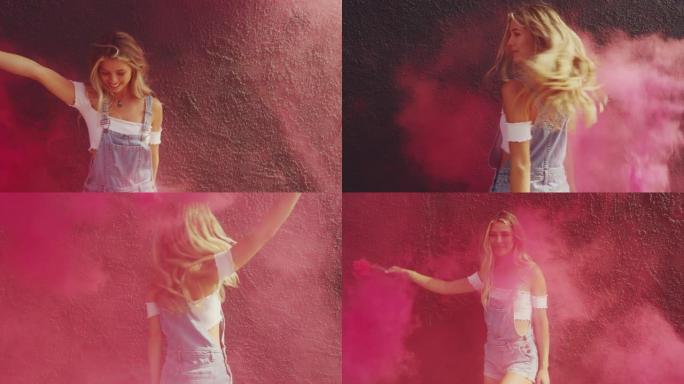 美丽的年轻金发女孩与粉红色烟雾弹对着黑墙跳舞
