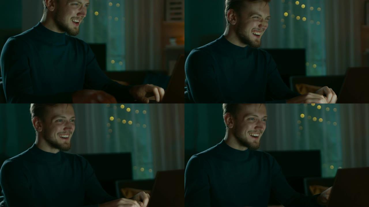 晚上在家: 英俊的微笑和大笑的男人坐在办公桌前在笔记本电脑上工作的肖像。微笑的自由职业者在电脑上工作