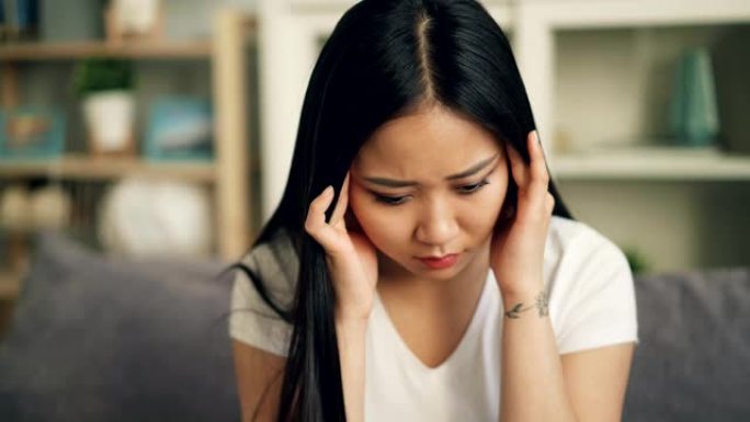不快乐的亚洲女学生头痛并试图释放疼痛，用悲伤的脸按摩头部触摸太阳穴。病态青年概念。