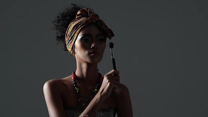 美丽性感的黑人女性，年轻漂亮的时尚模特，带有传统的非洲风格，深色背景上的围巾，耳环和化妆。黑色后台上