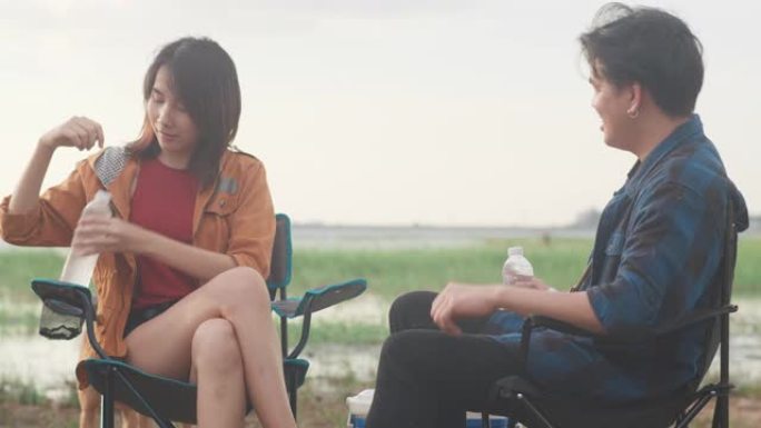 年轻的亚洲露营者夫妇坐在海边帐篷旁的椅子上。