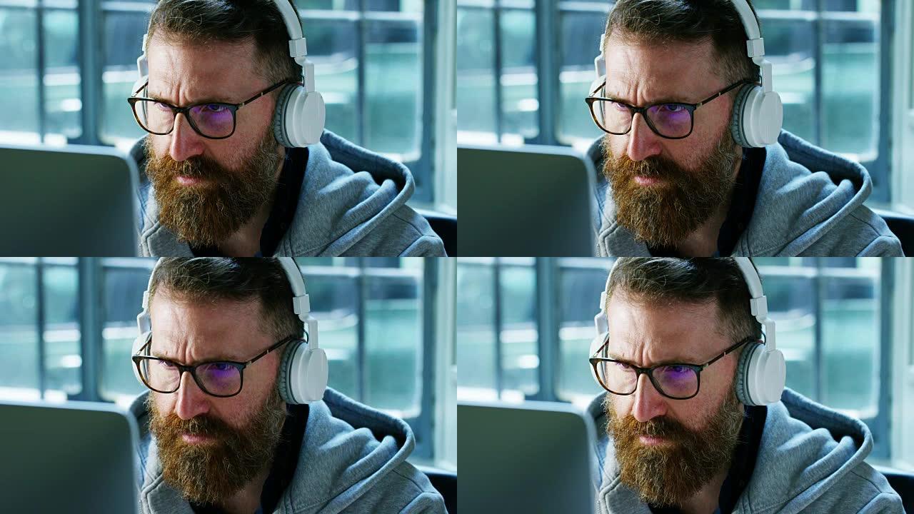 一个在计算机上工作的人微笑着，仔细地看着，为笔记本电脑上所做的工作感到自豪。催眠男孩专注于他的工作。