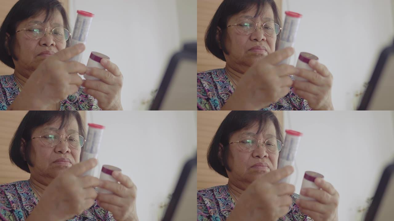 亚洲妇女拿着药瓶，在客厅里用平板电脑聊天。