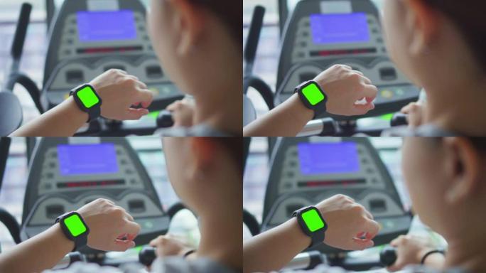 高清慢动作: 女人在健身房锻炼身体，看着智能手表，绿屏