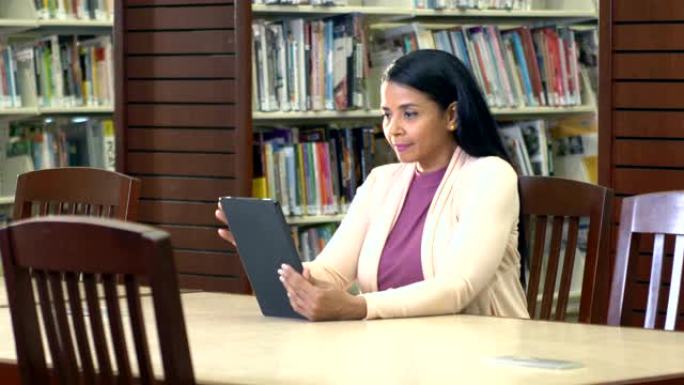 成熟的西班牙裔女性在图书馆阅读电子阅读器