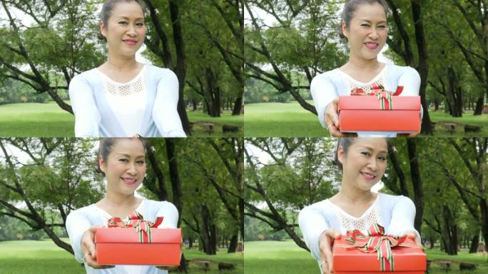 亚洲高级女性的特写镜头给相机后面的操作员礼物盒子。女人送礼物。