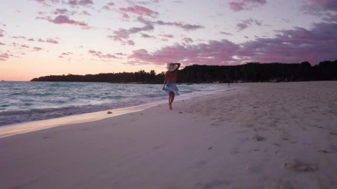 在美丽的白色海滩上奔跑，跳舞并玩乐的女人的鸟瞰图，周围是清澈晶莹的大海。