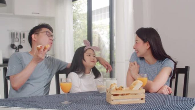 亚洲日本家庭在家里吃早餐。亚洲妈妈，爸爸和女儿在一起聊天很开心，早上在厨房的桌子上吃面包，玉米片谷物
