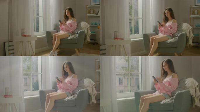 美丽的年轻女子坐在椅子上微笑着使用智能手机。性感的女孩穿着可爱的粉色毛衣和短裤，上网冲浪，在社交媒体