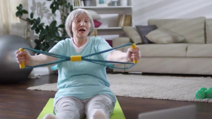 老年妇女用松紧带锻炼和观看视频锻炼