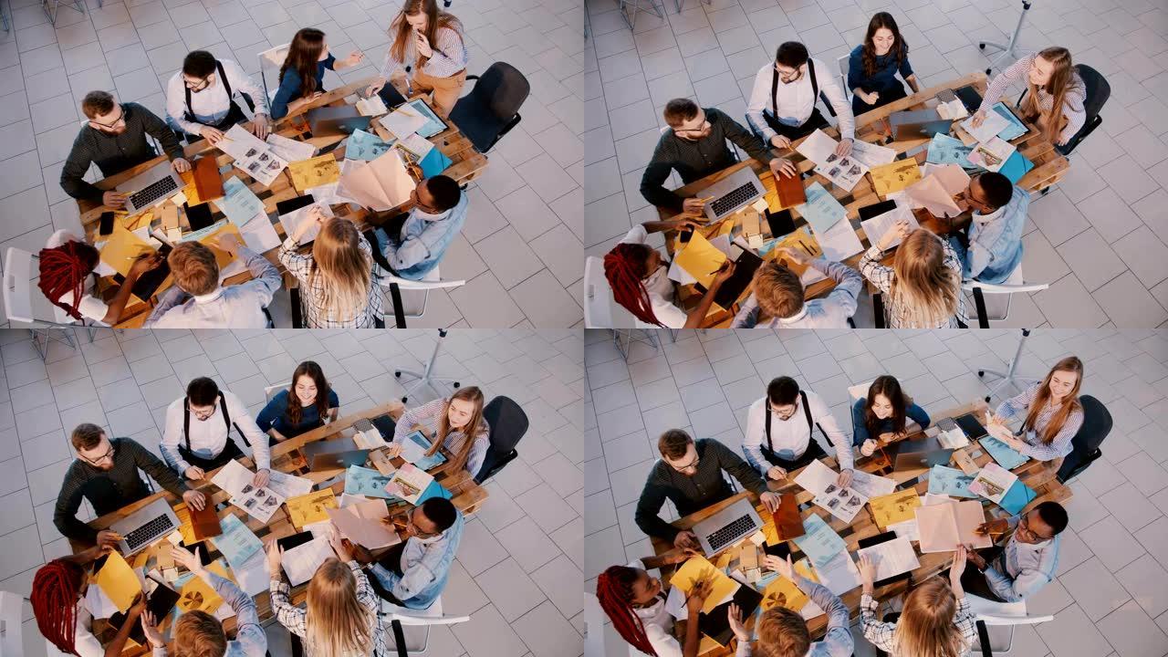 俯视图，快乐的专业商务人士团队合作在轻型现代办公室，年轻的女商人领袖讲话。
