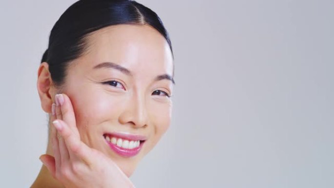 亚洲女人的慢动作，美丽的脸庞和完美的皮肤刚刚从杂质中清洗干净，用手轻轻地触摸它，以显示它是多么柔软和
