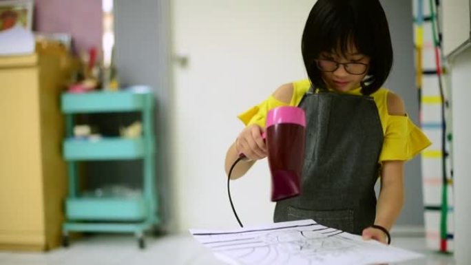 一名亚洲中国年轻女学生在美术课结束后用吹风机干掉水彩画