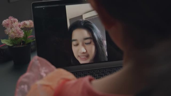 亚洲女孩使用笔记本电脑进行视频通话，并在家里的客厅与姐姐微笑，冠状病毒处于锁定状态，远离距离。技术和
