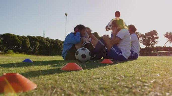 女足球运动员做仰卧起坐运动，而队长在足球场上进行训练。4k