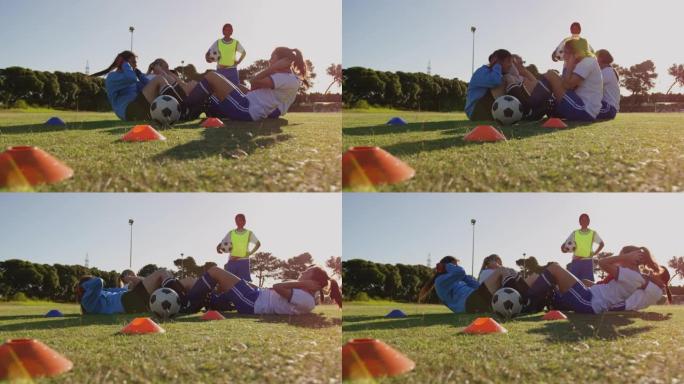 女足球运动员做仰卧起坐运动，而队长在足球场上进行训练。4k