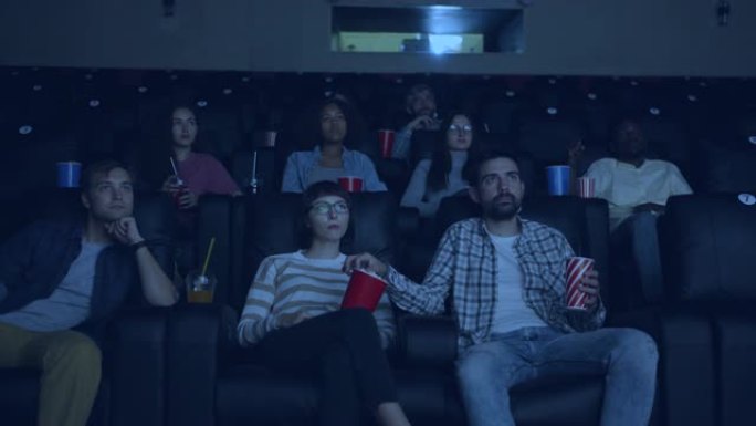 多种族的年轻人在电影院看电影吃喝