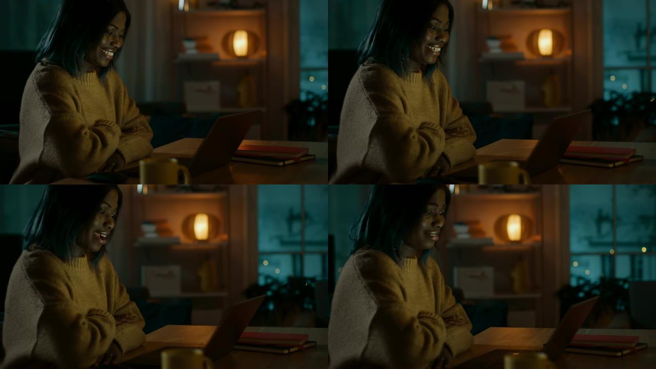 美丽微笑的黑人女孩的肖像坐在她的办公桌前，用笔记本电脑打视频电话，打招呼。晚上，女孩使用计算机网络摄