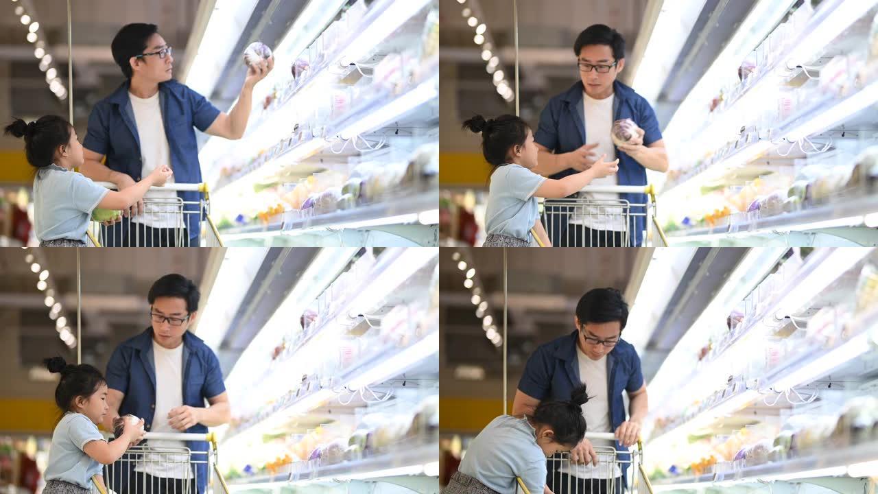 一对亚洲华人父亲和女儿在杂货店的冰箱蔬菜部挑选和购买蔬菜