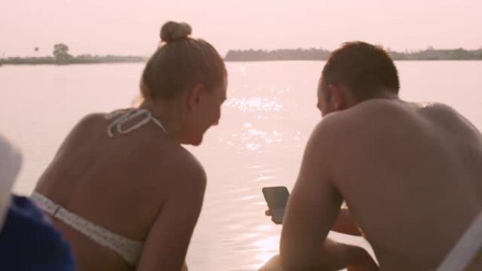 SLO MO夫妇在日落时在湖边放松时使用手机