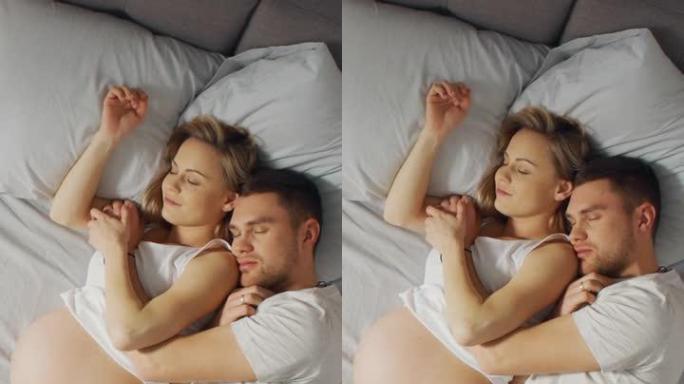 幸福的年轻夫妇与孕妇一起睡在床上，甜蜜的年轻人在睡觉时互相抱着。垂直屏幕方向9:16的视频素材