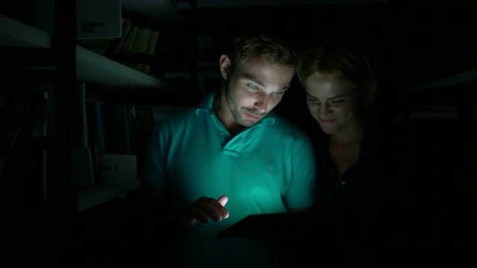 年轻夫妇走进图书馆的书架之间，看着平板电脑上的东西说话