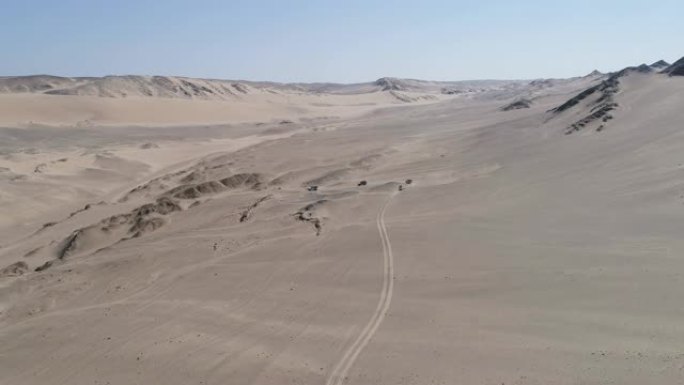 纳米比亚纳米布沙漠骨架海岸上4x4车辆在沙丘和山脉之间行驶的车队的4k空中后视图