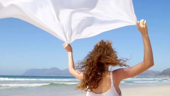 女人站在海边，挥舞着围巾。在海滩4k