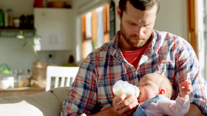 中年白人父亲在舒适的家庭4k中从奶瓶里给婴儿喂奶的前视图