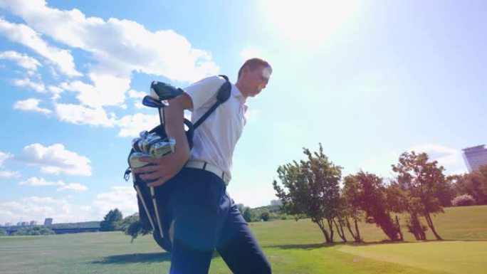 一个人拿着一个装有球杆的袋子，在高尔夫球场上散步。