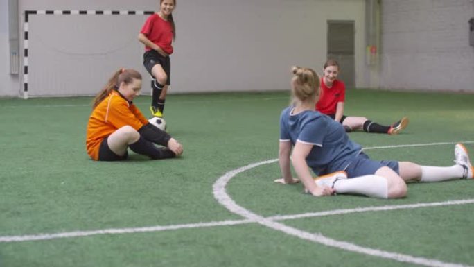 年轻的女足球运动员在室内场地聊天和伸展运动